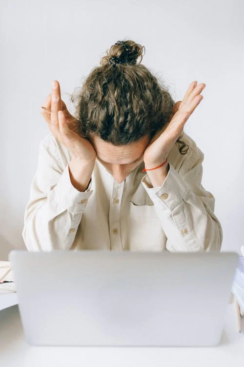 person in front of laptop with their head in their hands